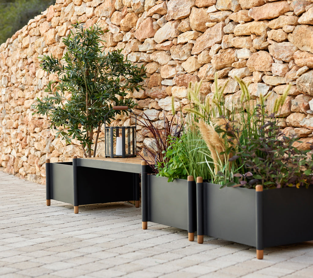 Un banc élégant avec deux jardinières remplies de verdure, accompagné d'une lanterne, placé contre un mur en pierre.