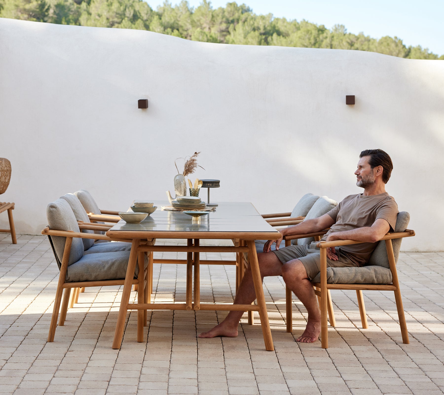 Un aménagement de salle à manger en teck avec une longue table et des chaises confortables, avec une personne assise, créant une atmosphère de repas détendue.