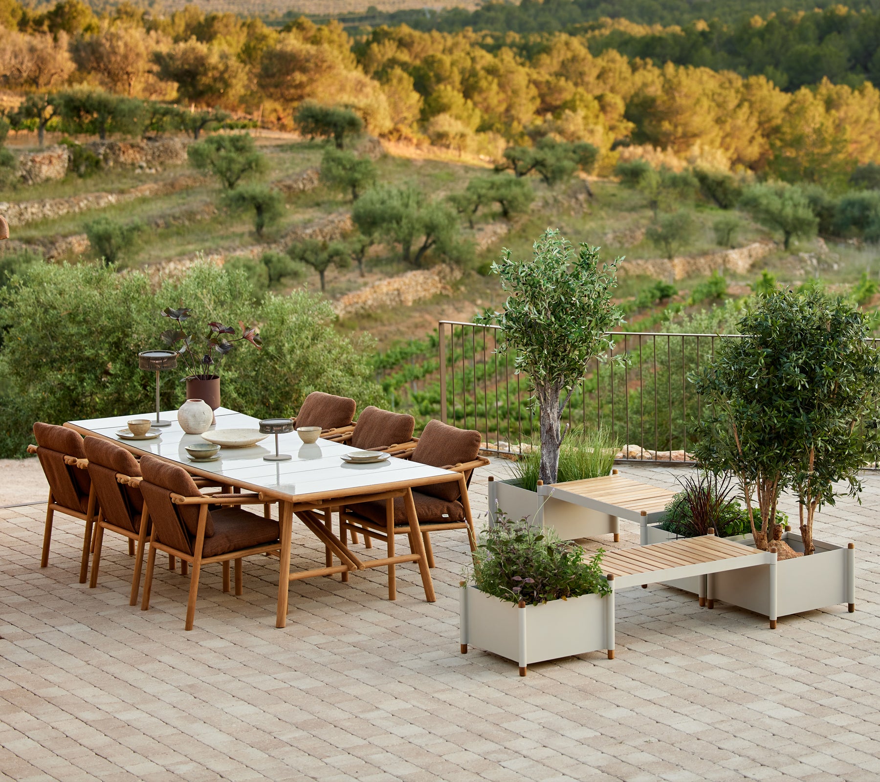 Ensemble de salle à manger en teck élégant avec chaises et banc à plantes, entouré de verdure et de paysage pittoresque.