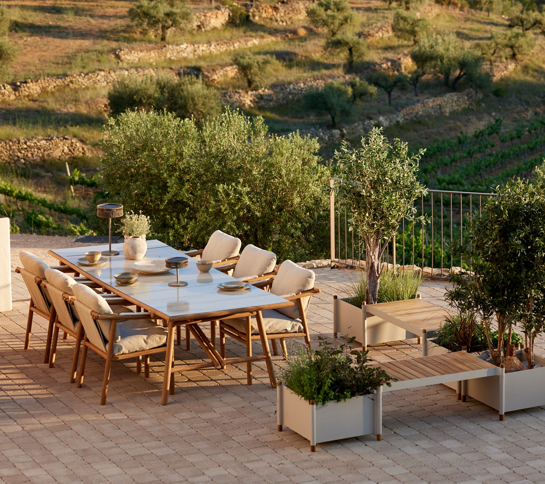 Un ensemble de salle à manger élégant avec des accents en teck, comprenant des chaises confortables et un banc à plantes, entouré de verdure.