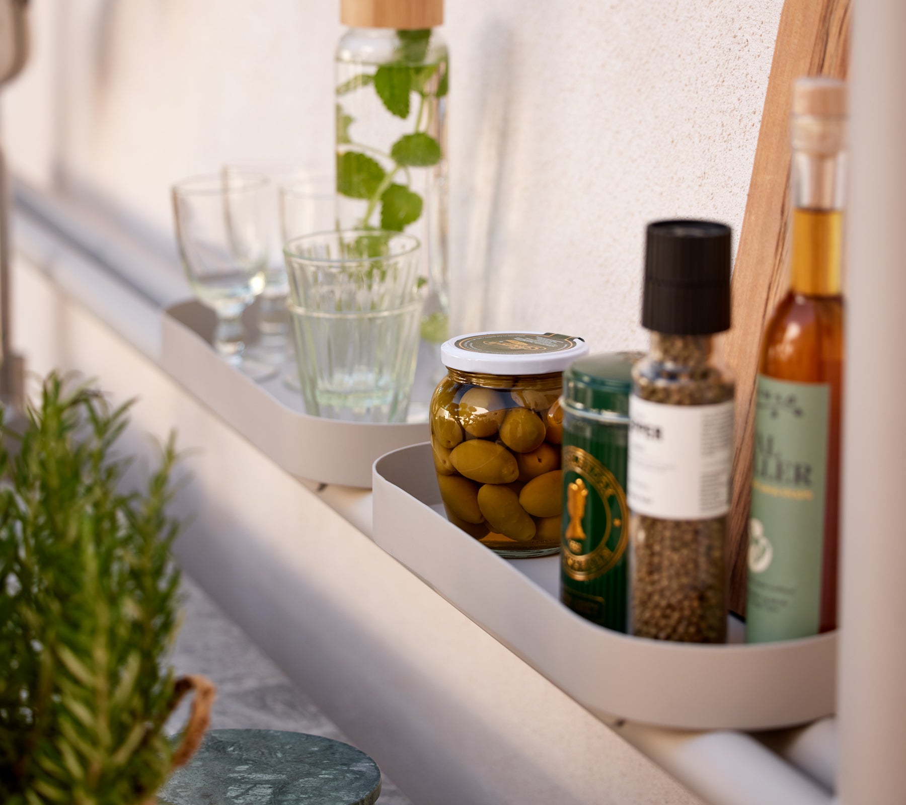Une étagère présentant divers articles de cuisine, y compris des verres, des bocaux d'olives et des bouteilles d'huile et d'épices.