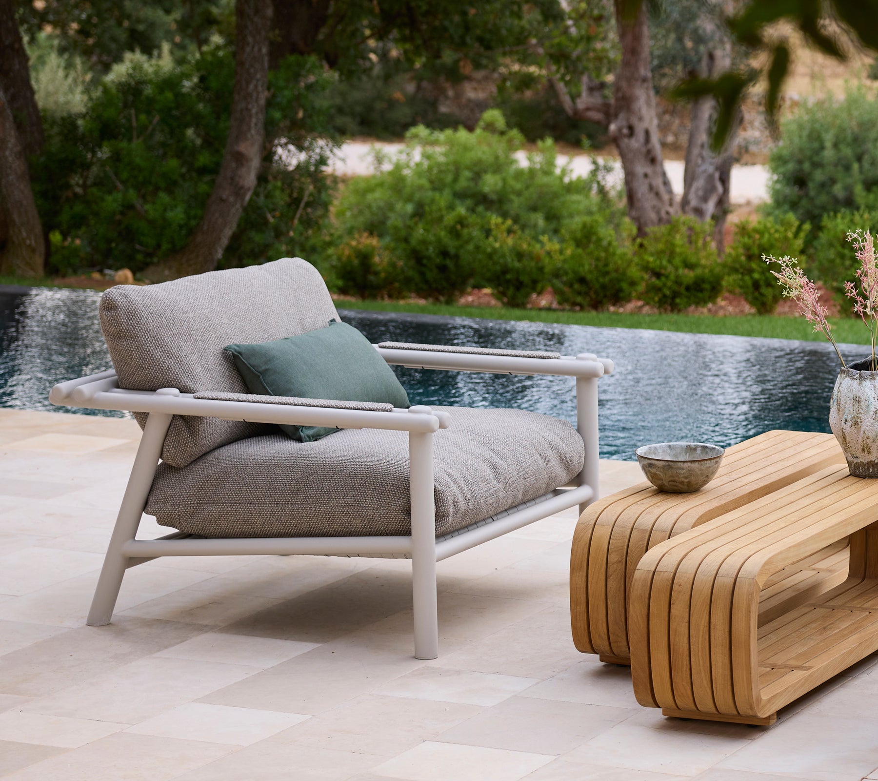 Environnement extérieur moderne avec un canapé gris, un coussin vert et une table basse en bois près d'une piscine.