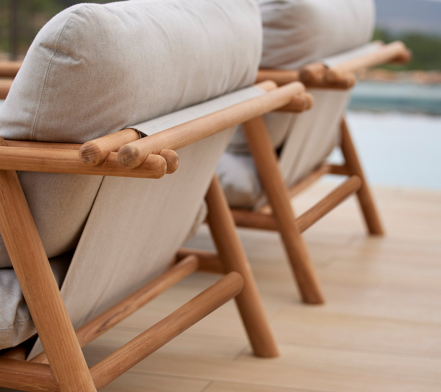 Deux fauteuils de salon élégants avec des cadres en teck et des coussins beiges confortables, présentant un design unique de tige sur le dossier.