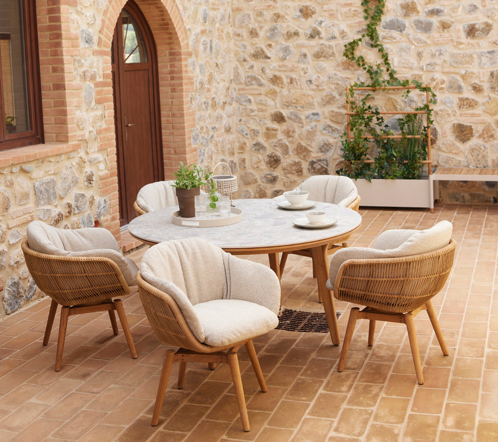 Un coin salon élégant composé de chaises arrondies et d'une table ronde, complété par de la verdure dans un pot contre un mur en pierre.
