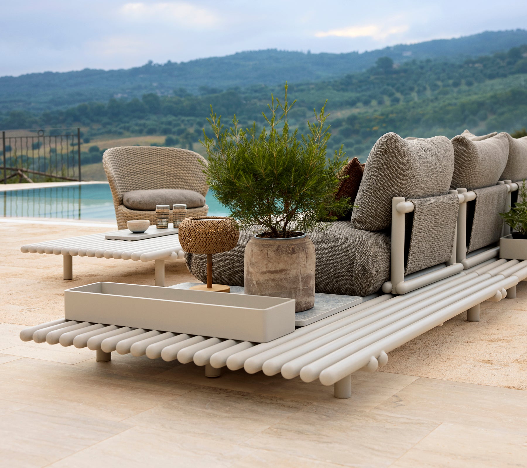 Un espace lounge élégant avec un fauteuil confortable, une boîte de rangement et une plateforme en aluminium, entouré de verdure.