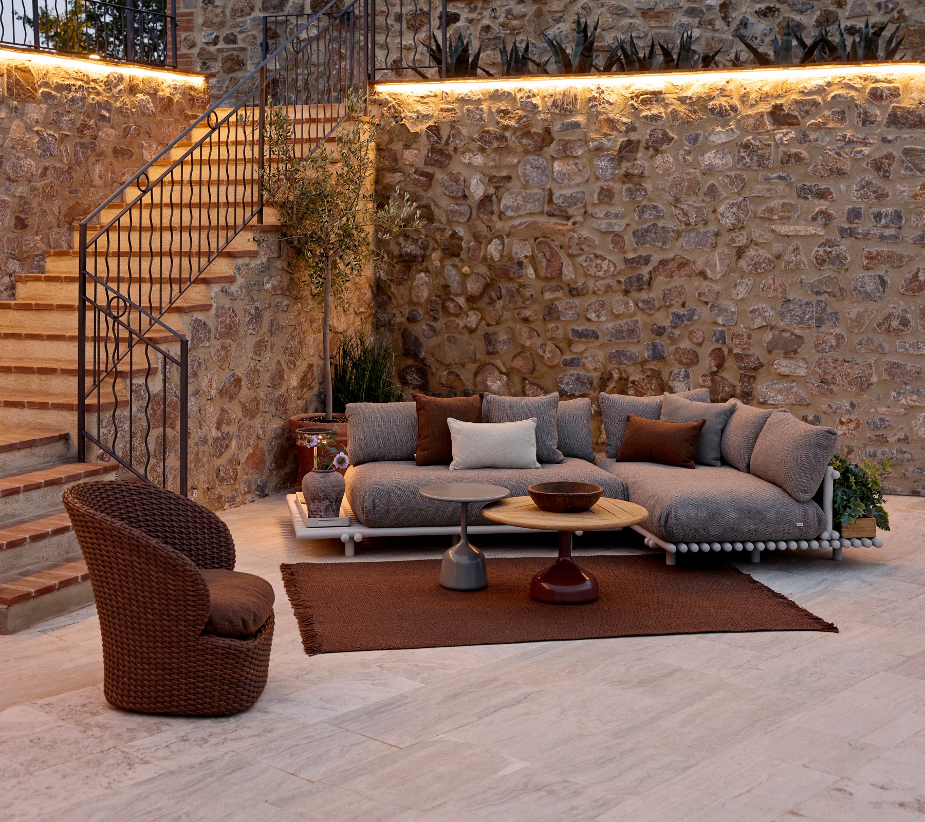 Espace salon confortable avec un canapé modulaire avec des coussins, une table basse ronde, un tapis tricoté et un fauteuil en osier.