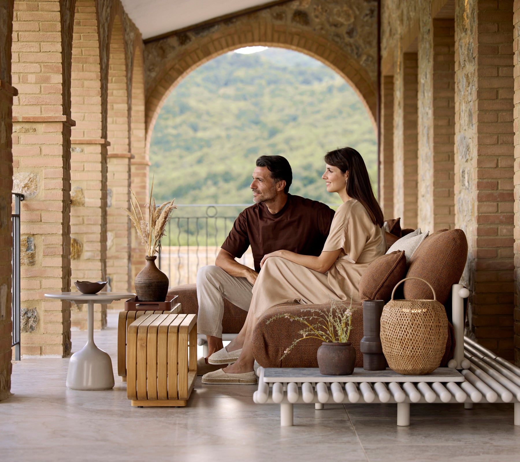 Un couple assis sur un canapé élégant, profitant d'une table basse Mellow avec des objets décoratifs et une vue sereine en arrière-plan.