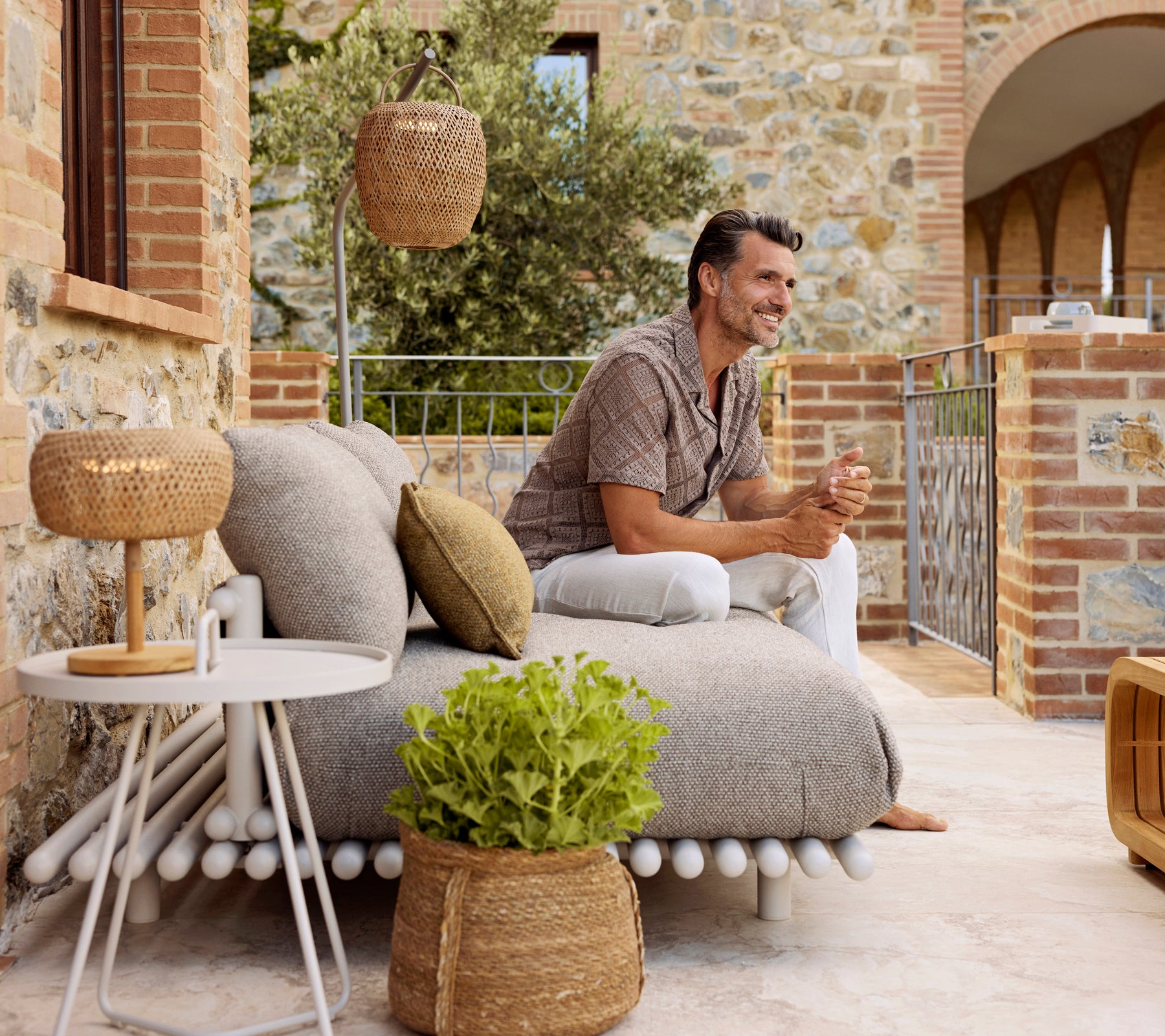 Un homme se détend sur un canapé confortable et texturé avec des coussins décoratifs, à côté d'une table d'appoint élégante et d'une lampe chaude et lumineuse.