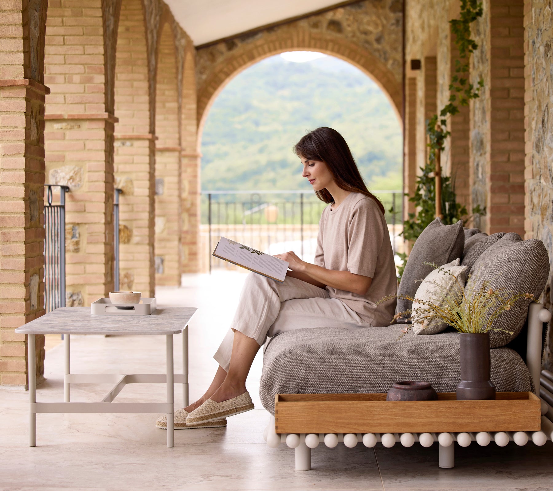 Une femme est installée confortablement en train de lire un livre à côté d'une table basse Twist rekt avec une boîte de rangement de style club, entourée d'éléments naturels.