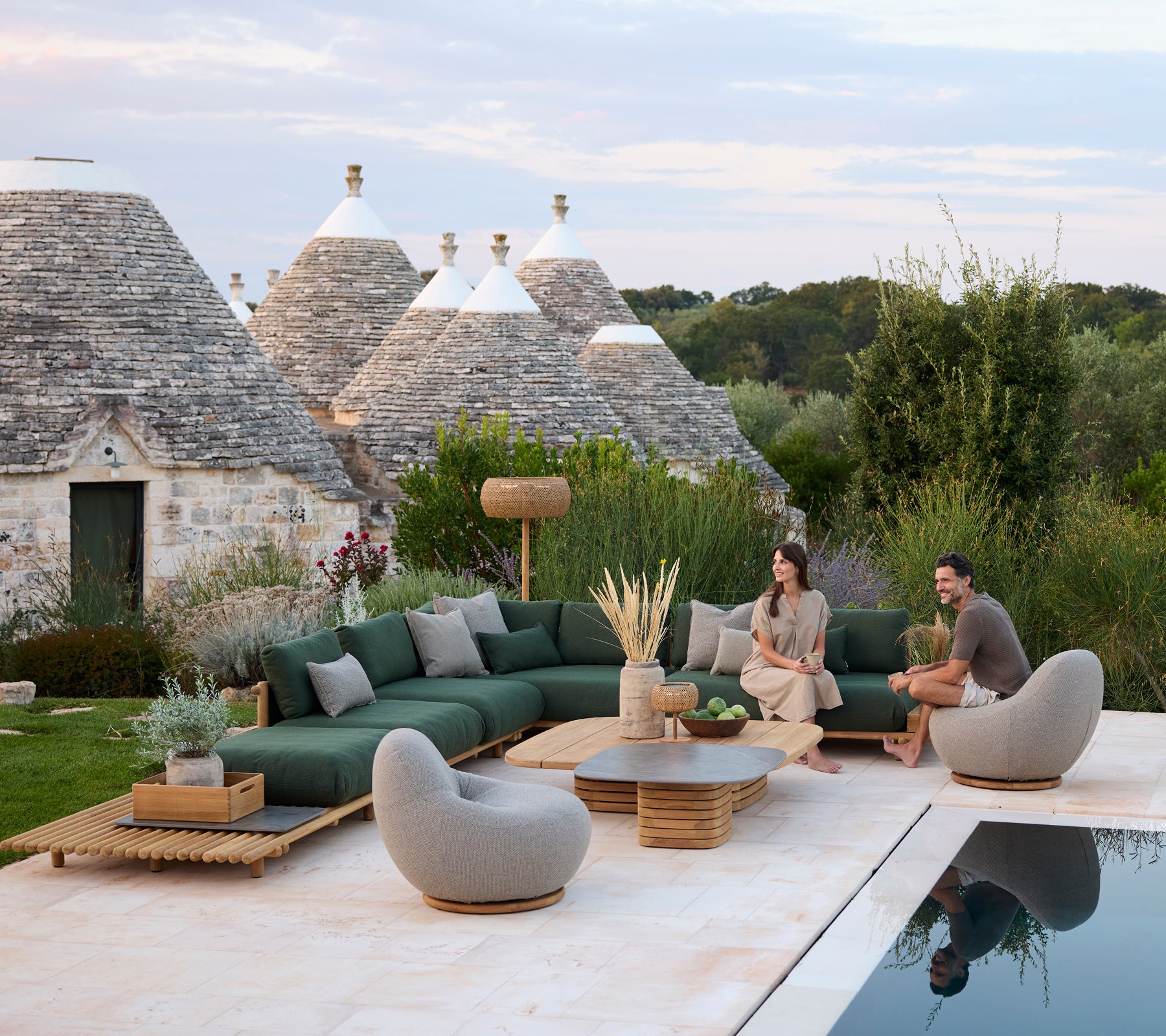 Espace lounge extérieur moderne avec un canapé sectionnel vert et des chaises grises au bord d'une piscine.