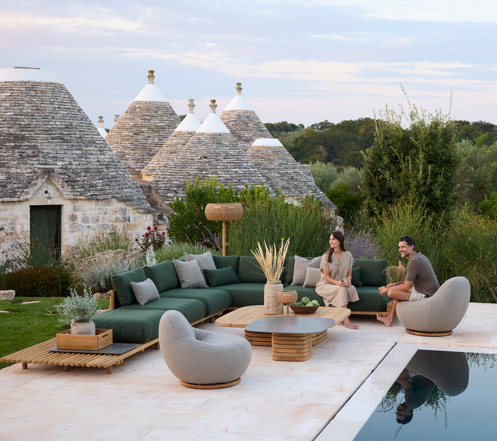 Espace lounge extérieur moderne avec un canapé sectionnel vert et des chaises grises au bord d'une piscine.