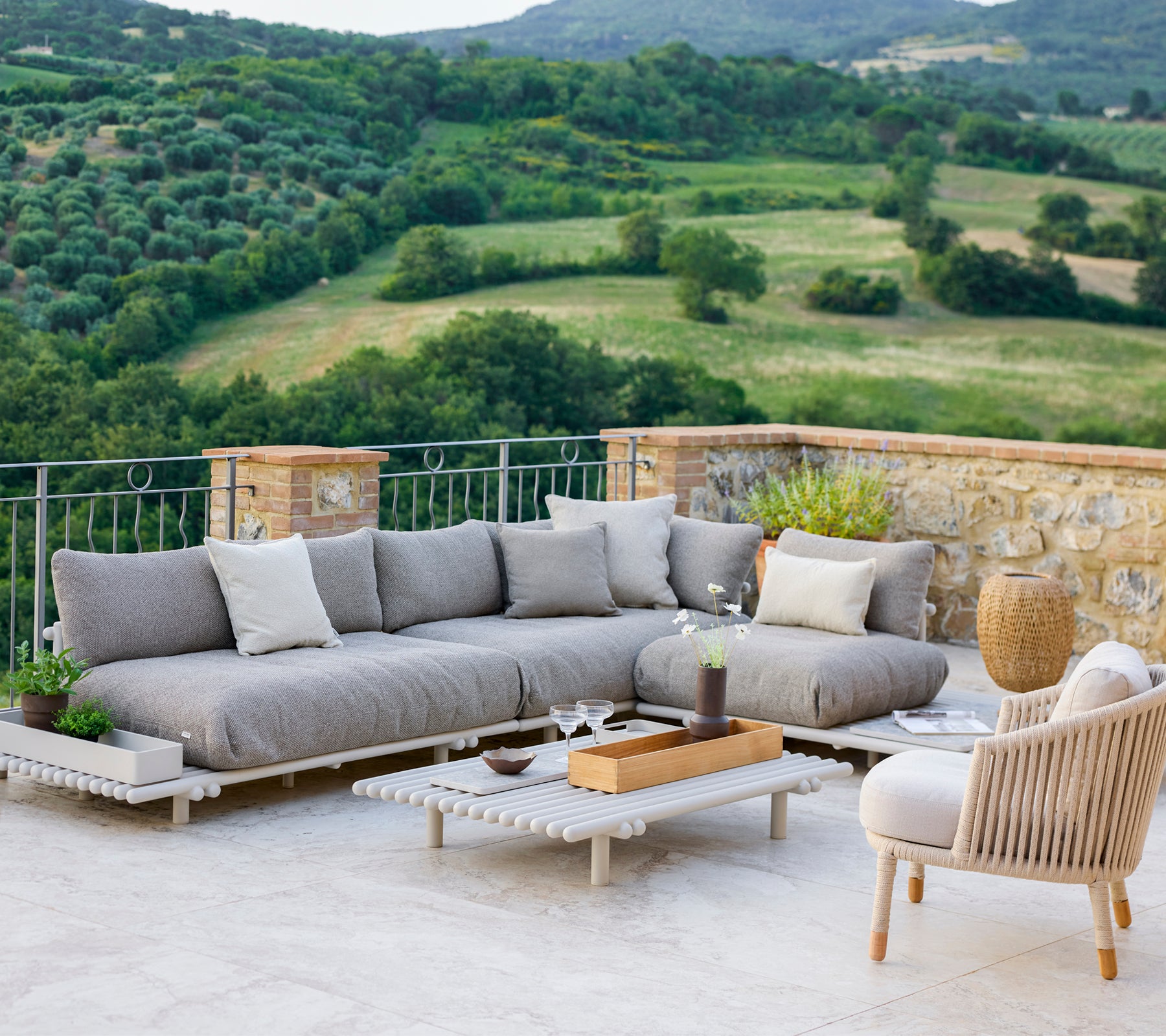 Espace lounge élégant avec un canapé sectionnel gris et une chaise confortable, situé face à un paysage pittoresque.