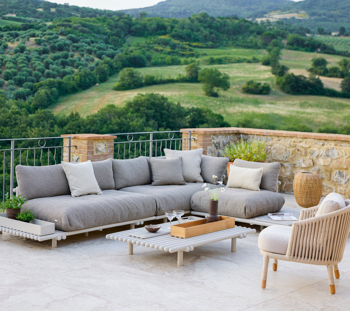Espace lounge élégant avec un canapé sectionnel gris et une chaise confortable, situé face à un paysage pittoresque.