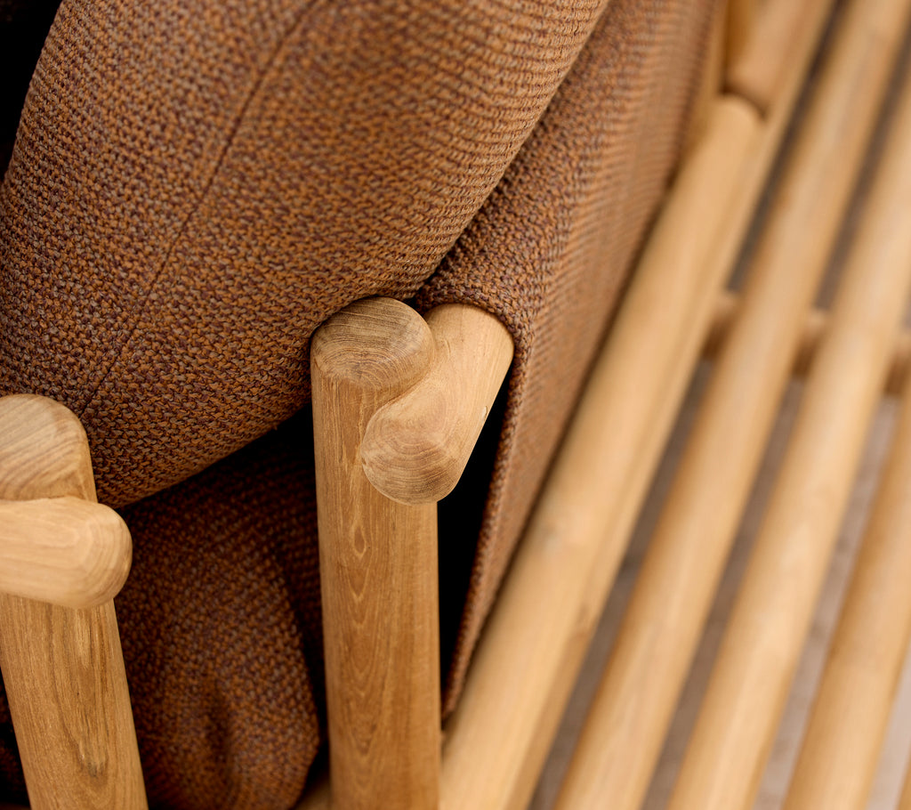 Chaise longue en teck avec des coussins doux et des tiges en bois élégantes formant l'accoudoir et la structure de base.