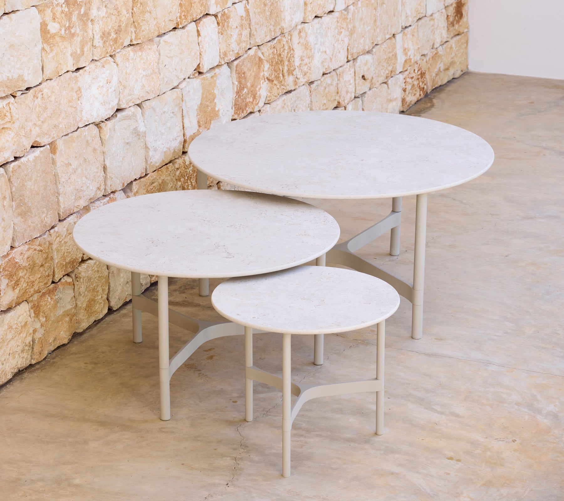 Trois tables rondes modernes de différentes tailles contre un mur en pierre.