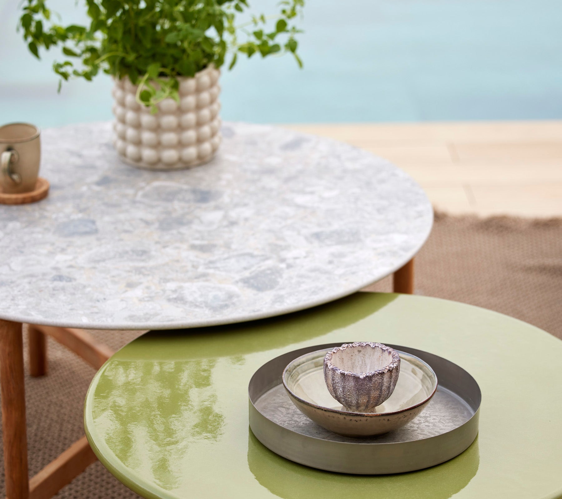 Une table Twist multicolore avec un plateau en pierre de lave émaillée, accompagnée d'un bol décoratif et d'une plante dans un cadre élégant.