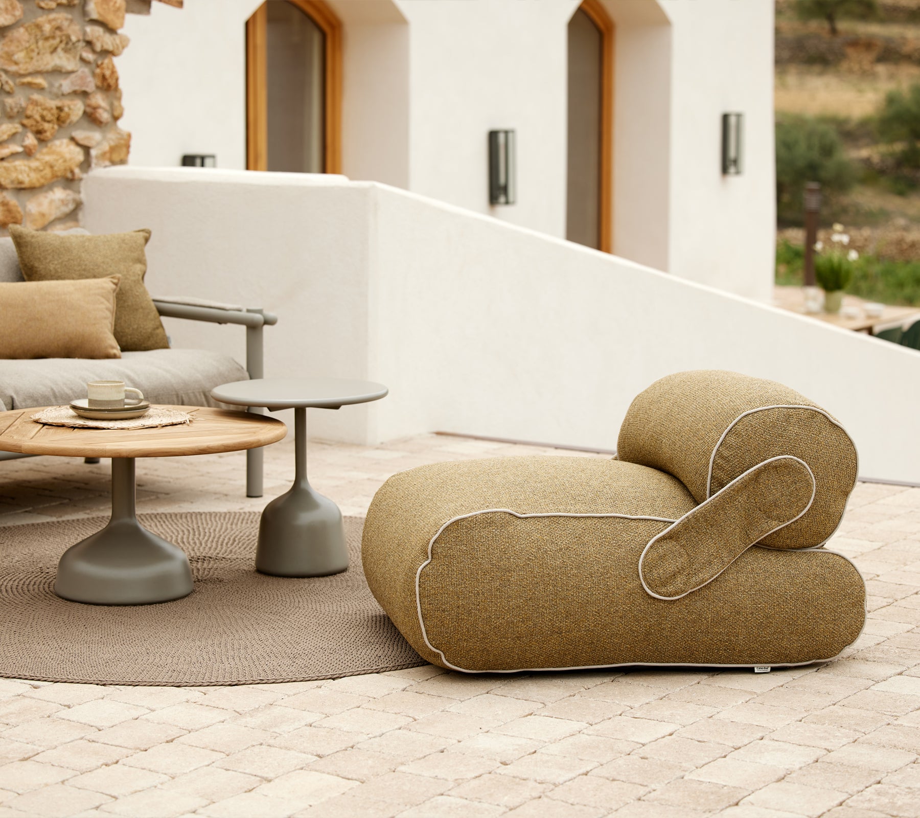 Fauteuil élégant avec une forme unique, accompagné d'une table ronde et de coussins décoratifs, situé dans un environnement paisible.