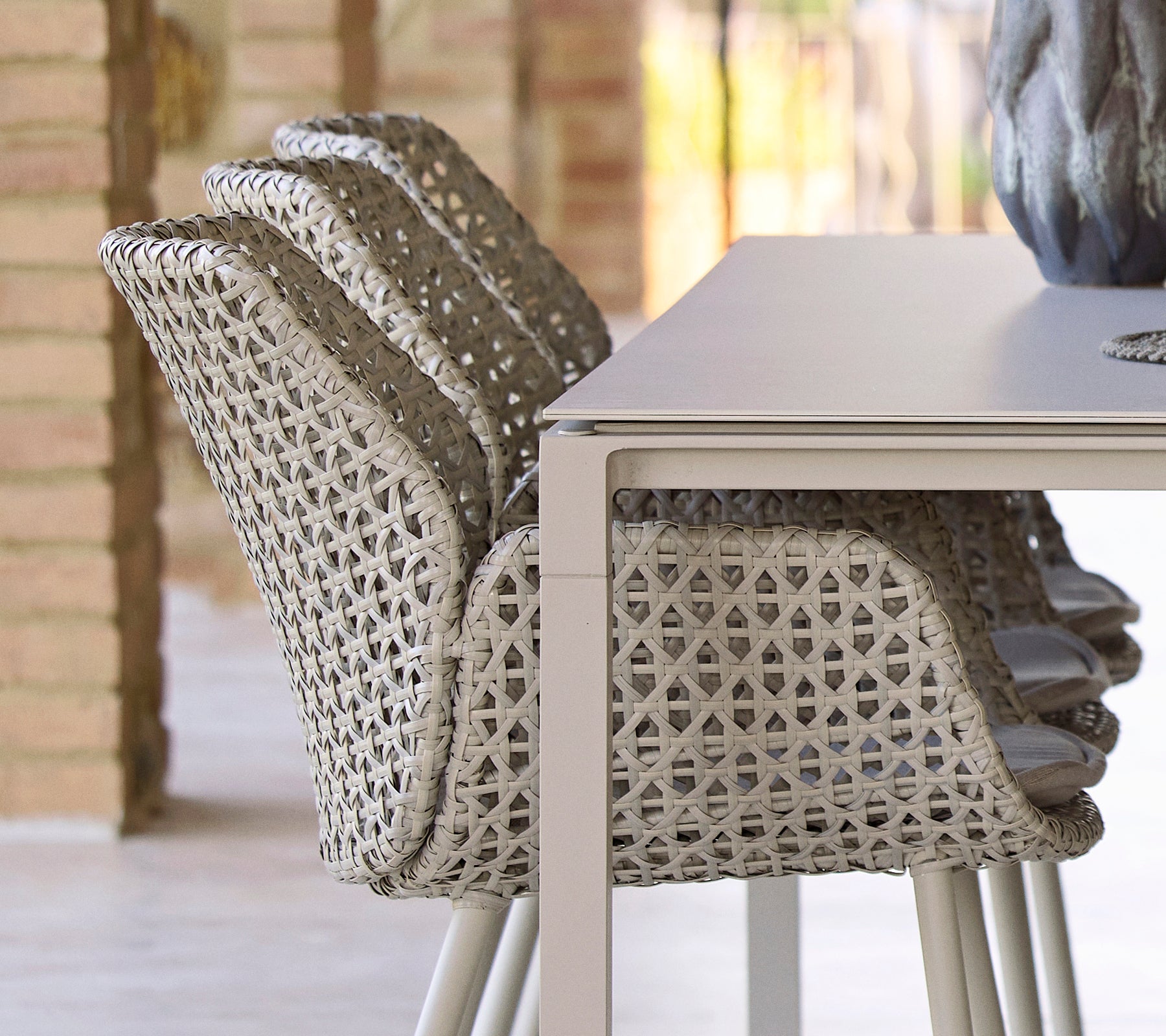 Des chaises empilées avec un design tissé unique à côté d'une table à manger lisse et minimaliste, créant un arrangement de repas moderne et accueillant.