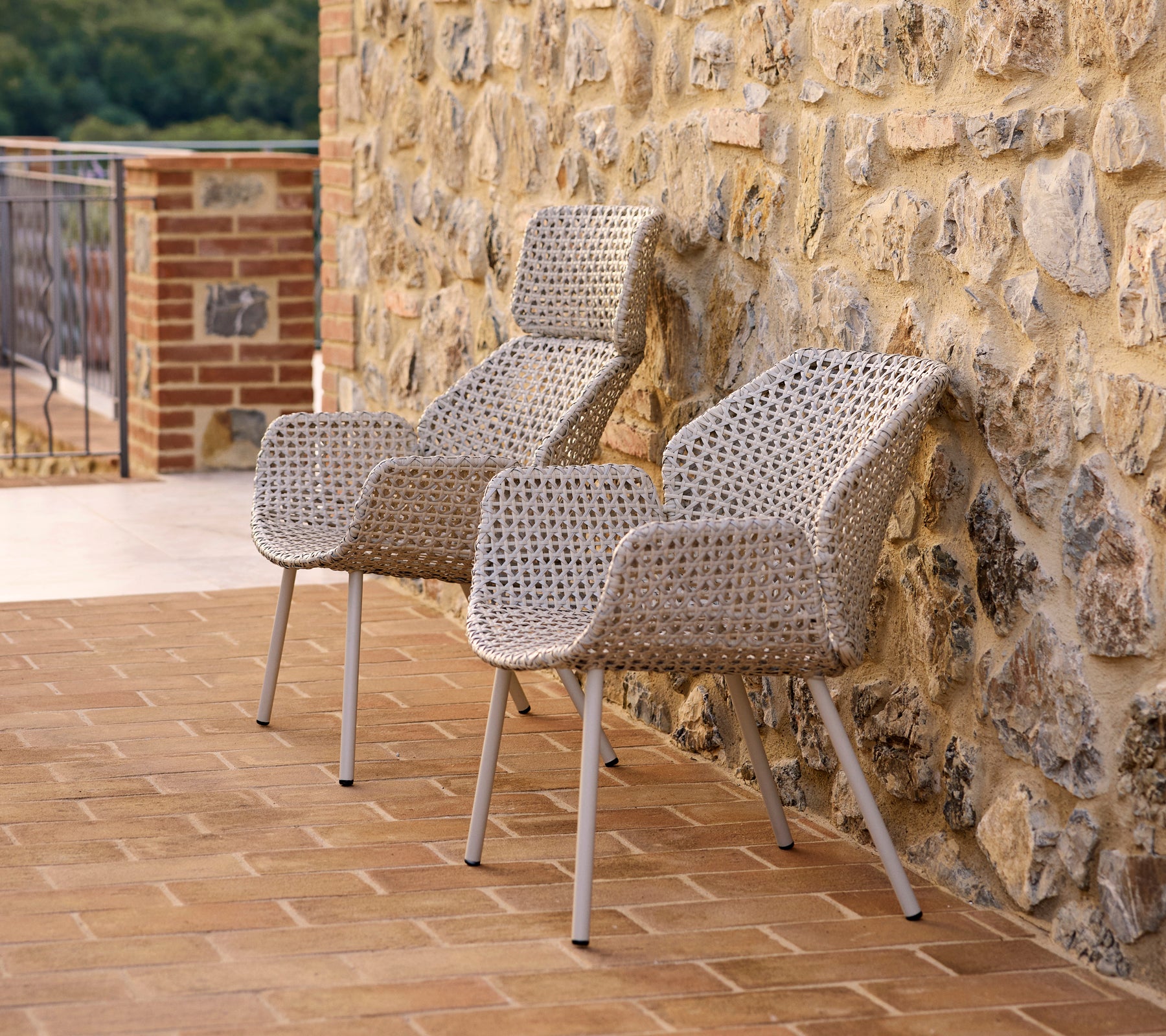 Deux fauteuils Vibe à dossier haut, en matériau tissé, positionnés contre un mur en pierre, parfaits pour se détendre.