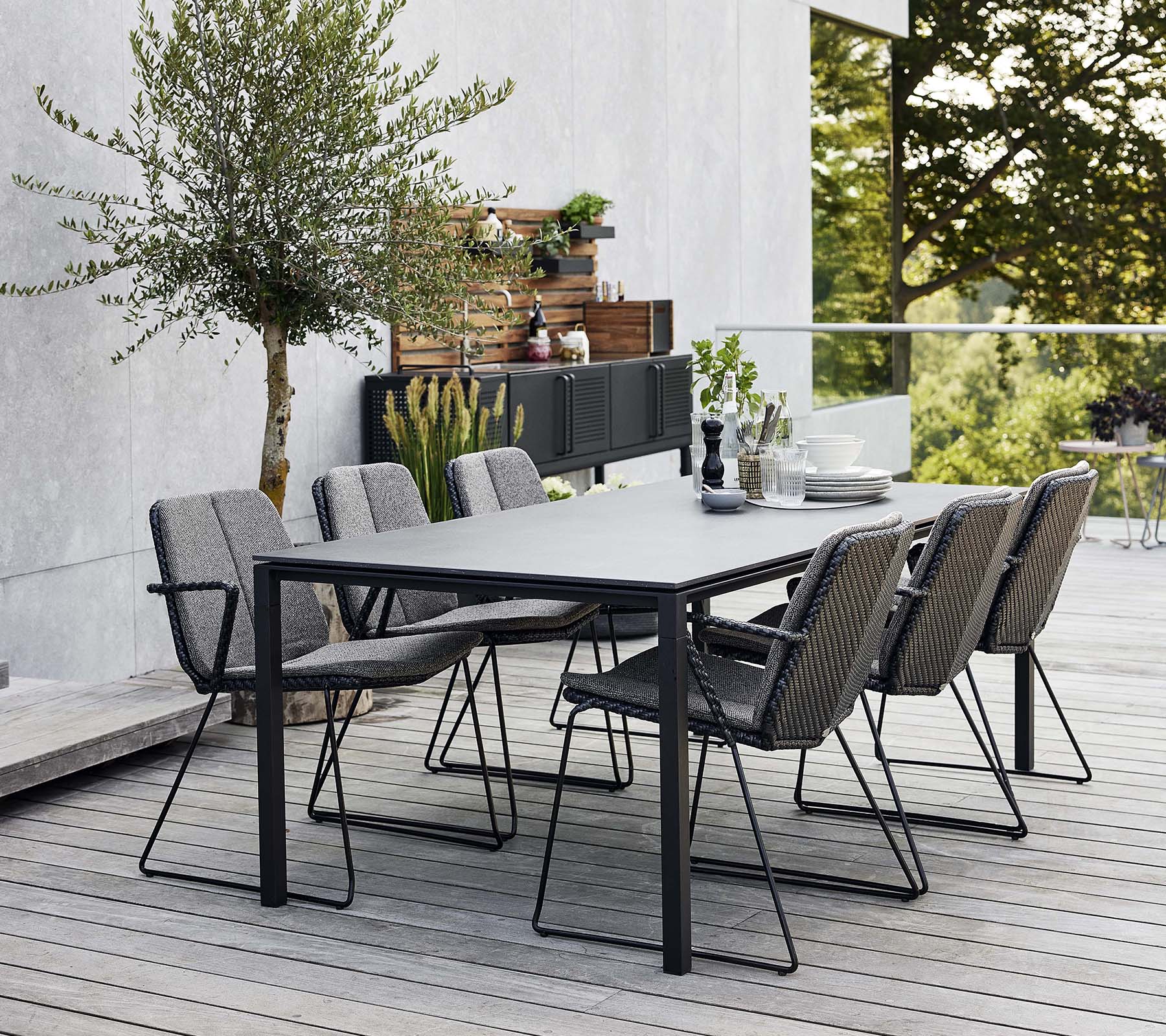 Un ensemble de salle à manger d'extérieur élégant avec une table épurée et plusieurs fauteuils confortables, entouré de verdure et d'un fond moderne.