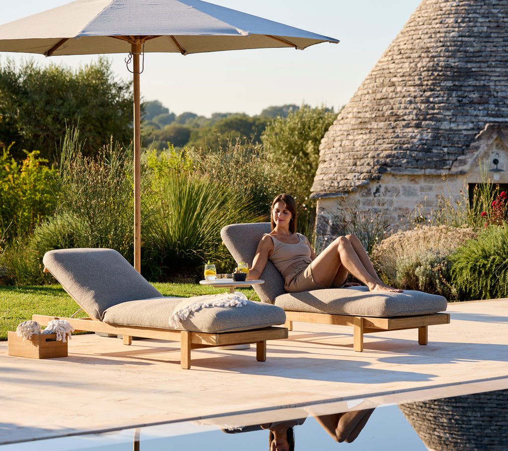 Deux chaises longues avec des coussins beiges sous un parasol dans un cadre extérieur serein.