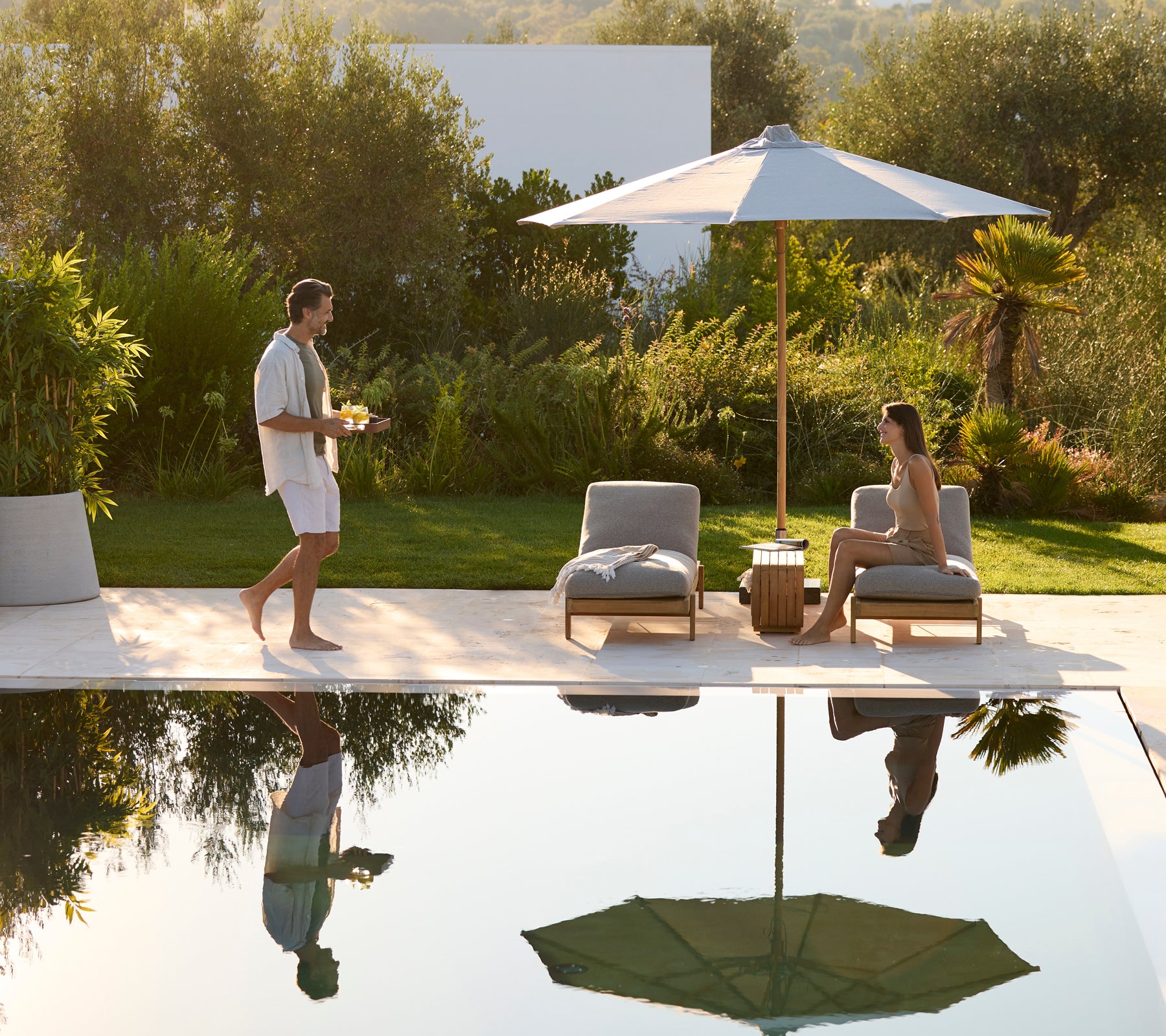 Espace lounge moderne en plein air avec des chaises grises, une table en bois et un parapluie vert.