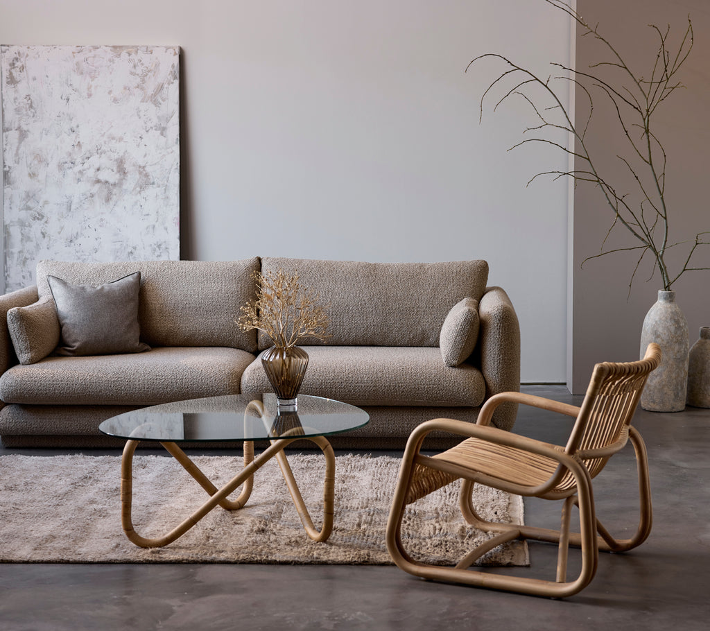 Aménagement contemporain du salon avec un canapé beige, une table en verre et une chaise en osier.