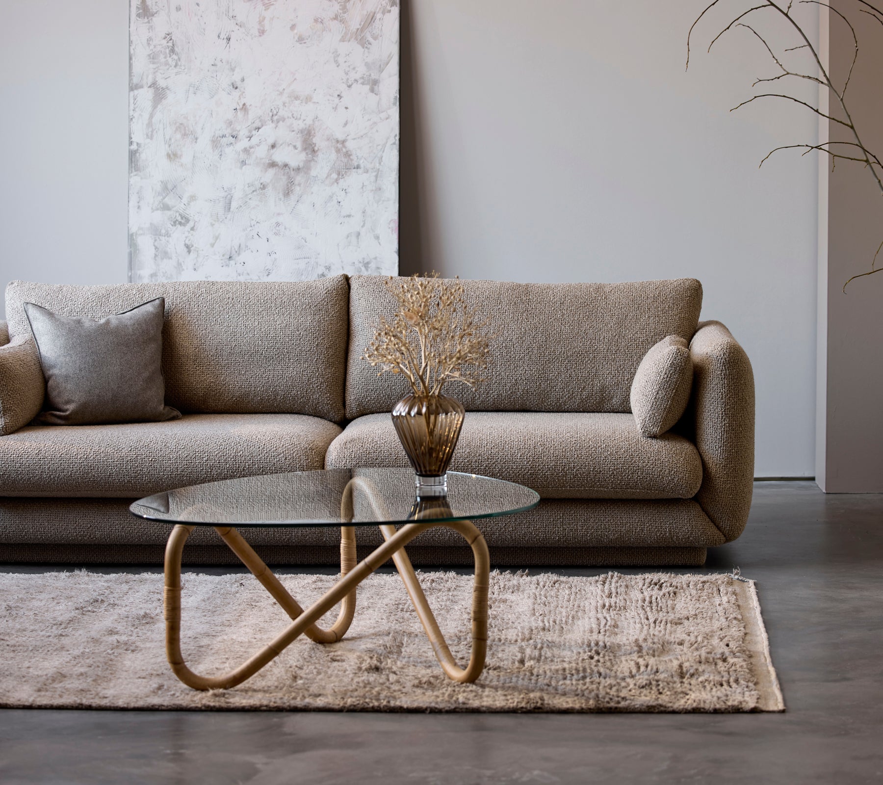 Un canapé beige moderne avec une table basse en verre et un vase décoratif dans un cadre de salon minimaliste.