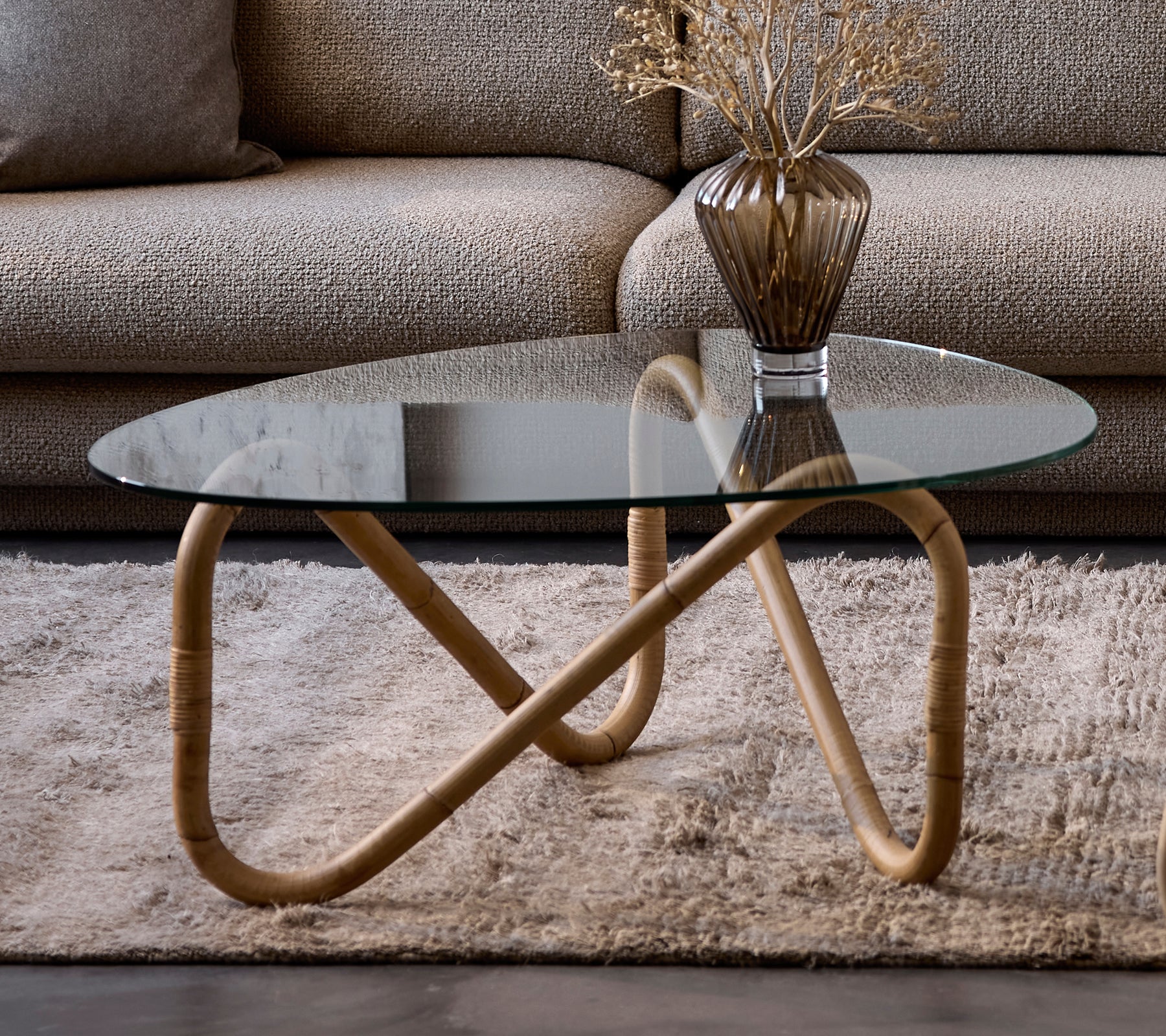 Table basse en verre moderne avec un vase beige sur un tapis dans un cadre de salon.