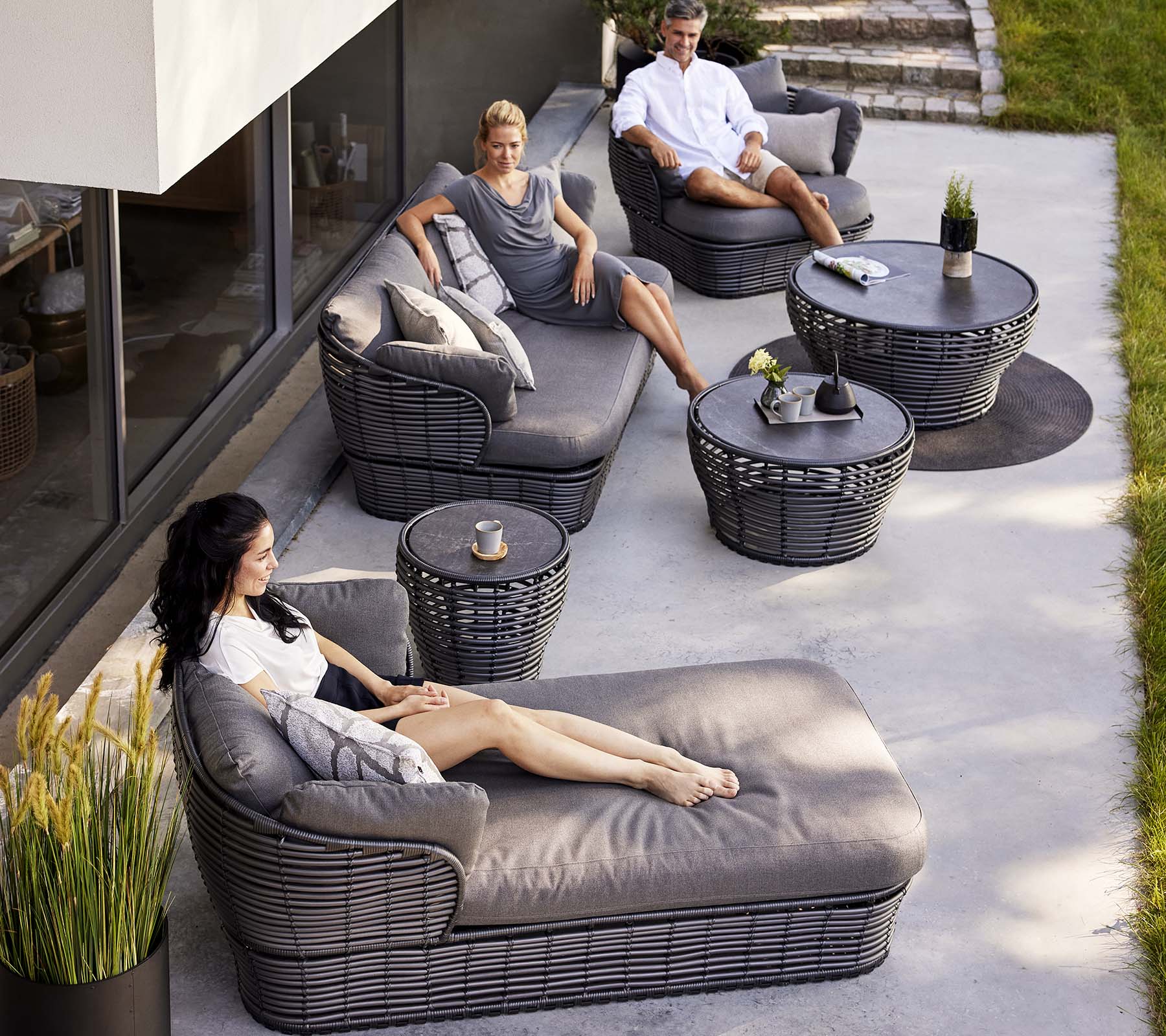 Espace lounge contemporain avec un lit de jour en osier, un canapé 3 places et des fauteuils, complété par des tables rondes et des plantes décoratives.