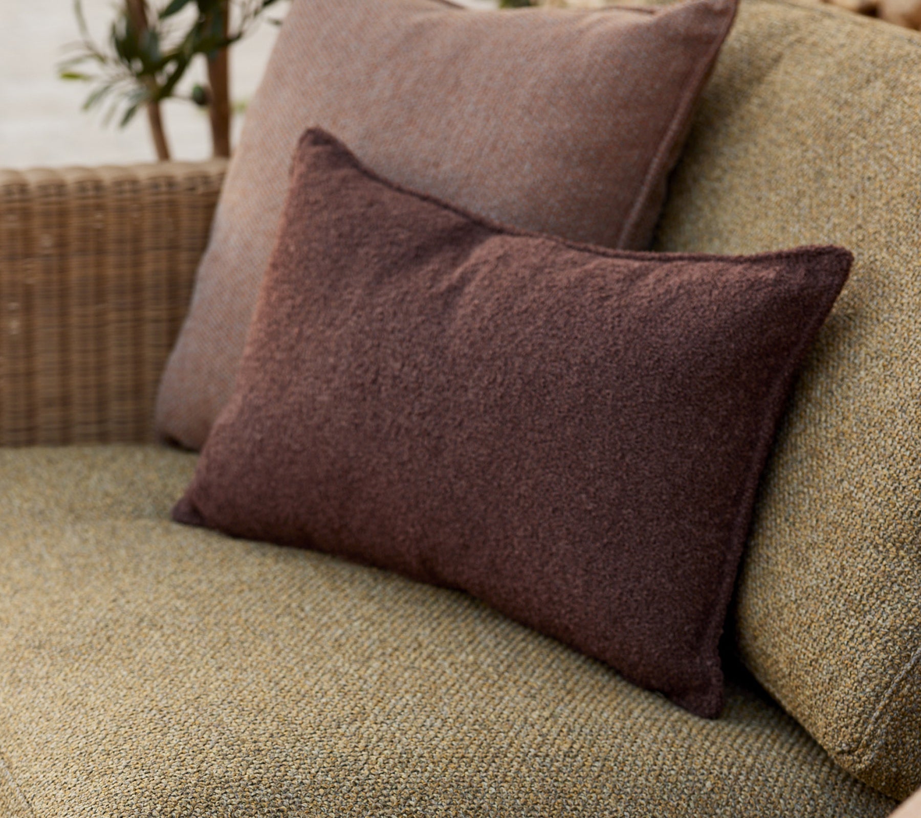 Des coussins décoratifs doux en tons terreux, disposés confortablement sur une surface tissée, ajoutant une touche chaleureuse à l'ensemble.