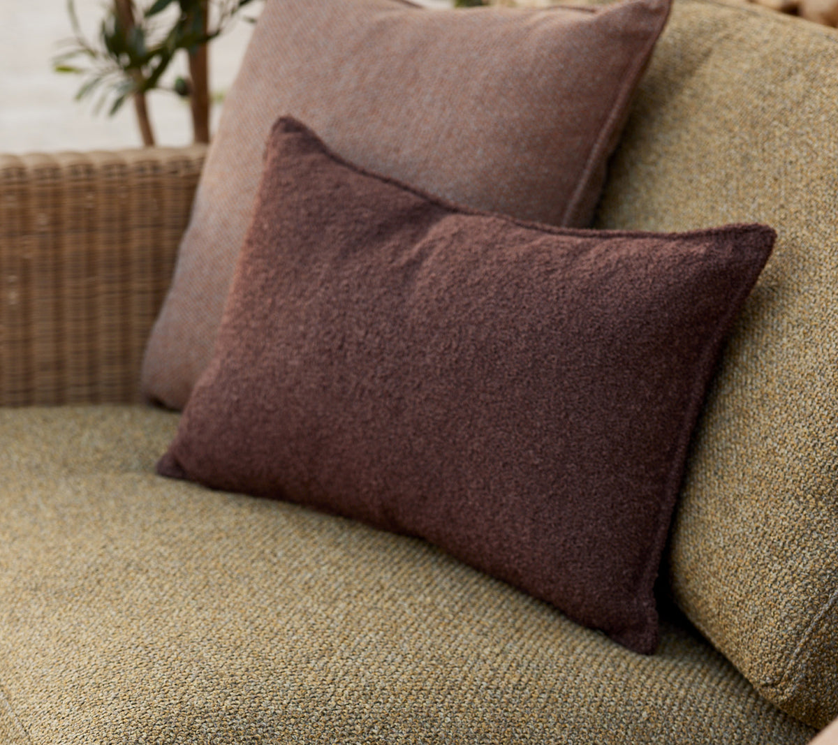 Des coussins décoratifs doux en tons terreux, disposés confortablement sur une surface tissée, ajoutant une touche chaleureuse à l'ensemble.