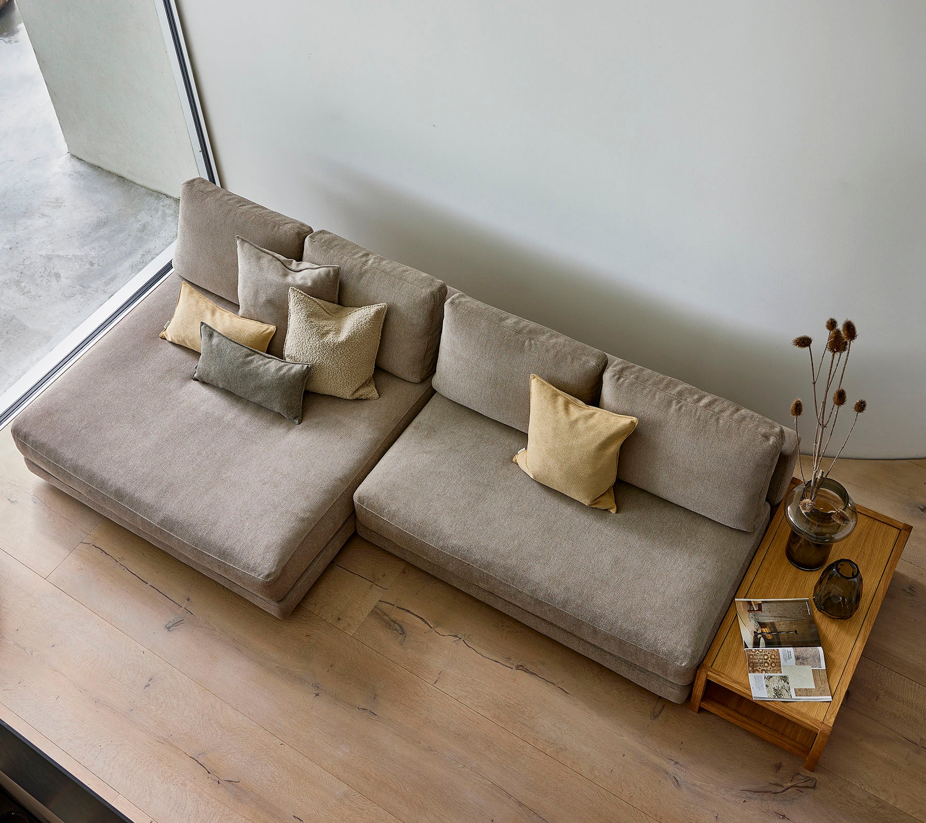 Un canapé élégant dans une teinte neutre, orné de divers coussins décoratifs, accompagné d'une table d'appoint en bois avec des livres et un vase.
