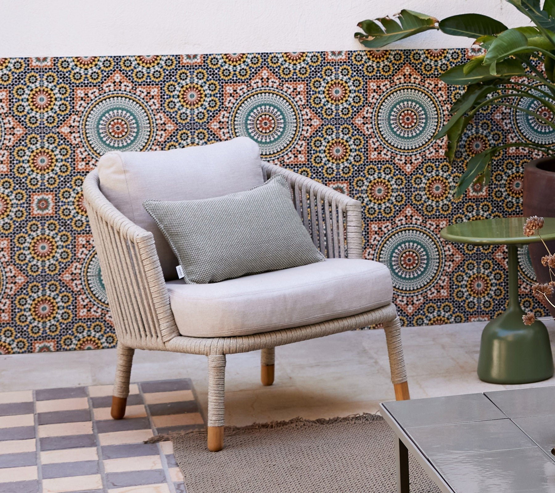 Un fauteuil lounge élégant avec un coussin doux et un coussin décoratif, placé devant un fond à motif et entouré d'une plante en pot.