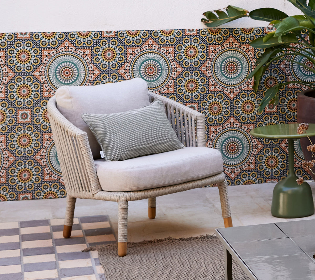 Un fauteuil lounge élégant avec un coussin doux et un coussin décoratif, placé devant un fond à motif et entouré d'une plante en pot.