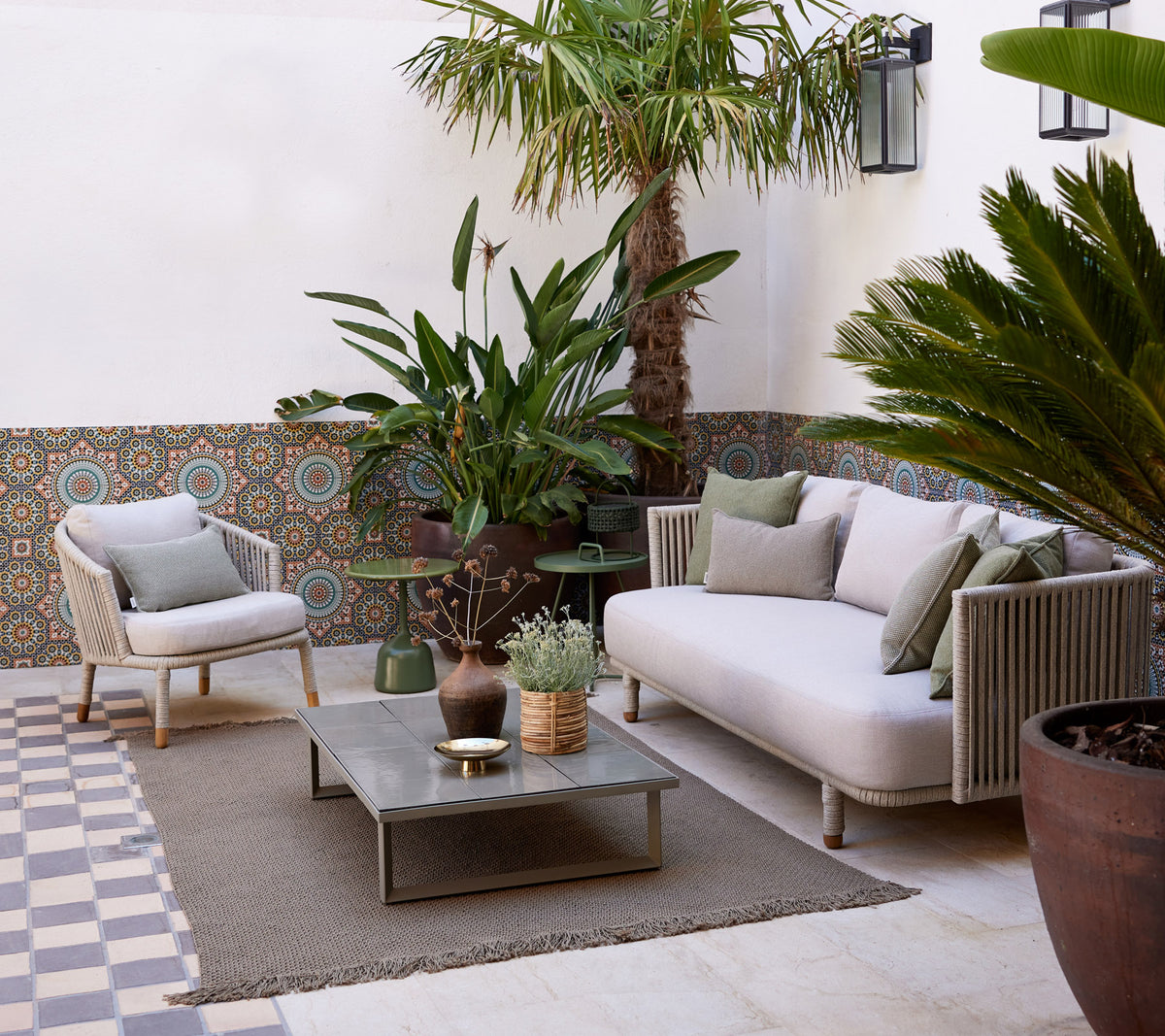Espace salon confortable avec un canapé clair, des plantes en pot, une table décorative et un sol texturé, créant une ambiance sereine.