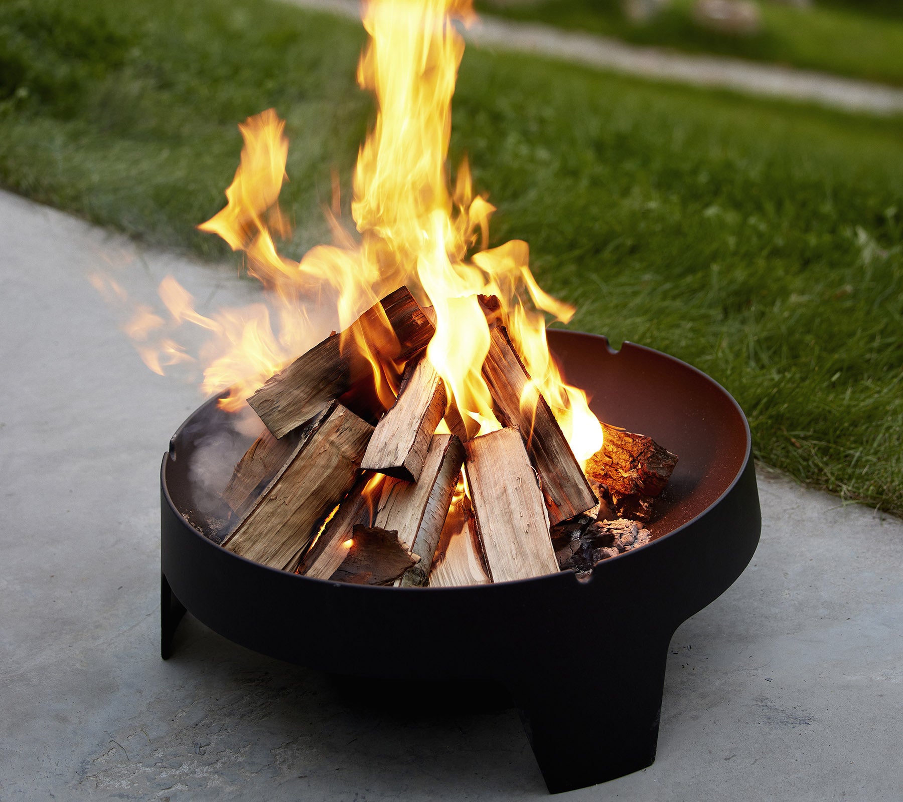 Un foyer de feu avec des flammes s'élevant au-dessus de bûches empilées, entouré d'herbe, créant une atmosphère chaude et accueillante.