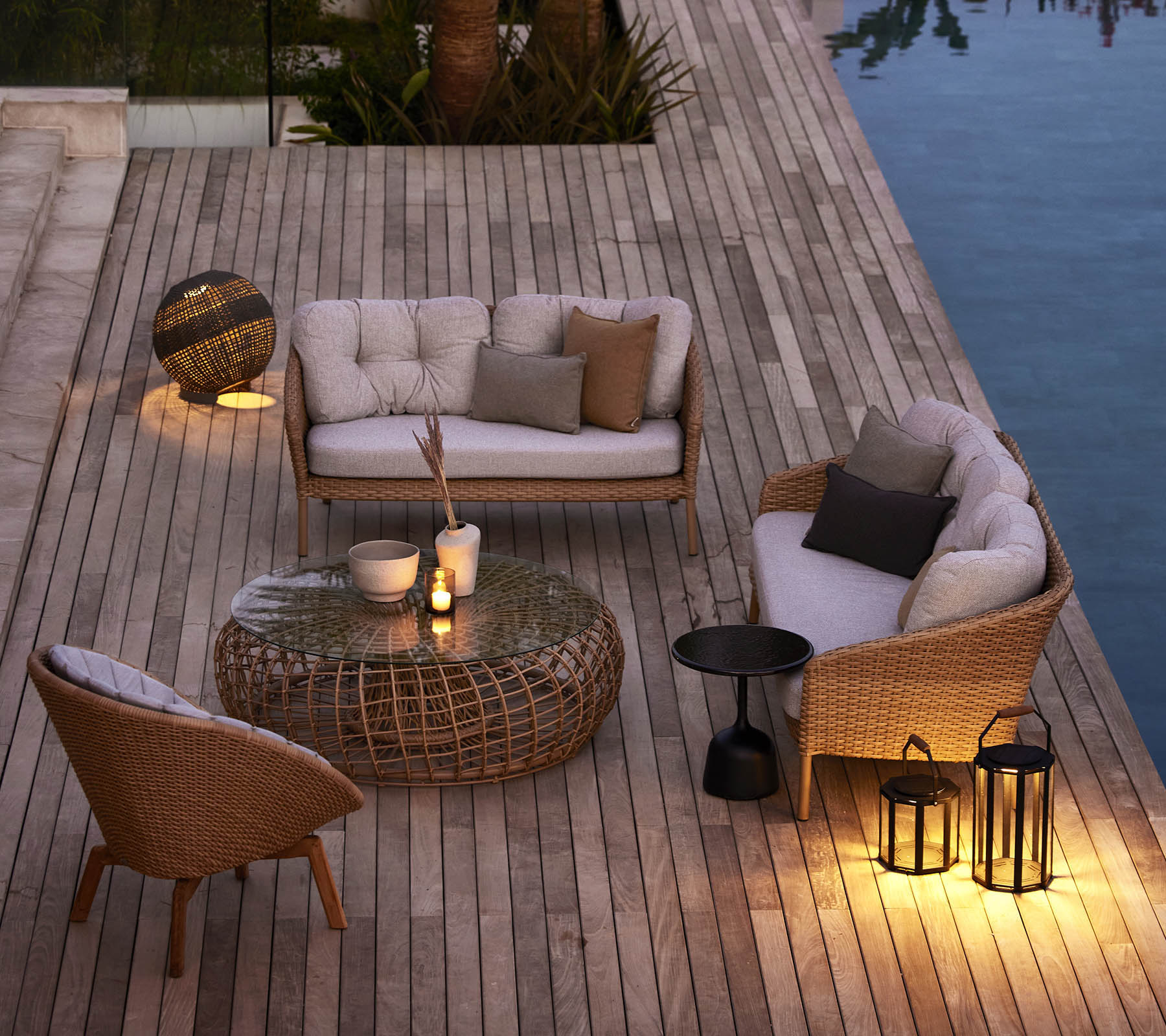 Espace extérieur confortable avec des meubles en osier, des coussins moelleux et un éclairage d'ambiance à côté d'une piscine sur une terrasse en bois.
