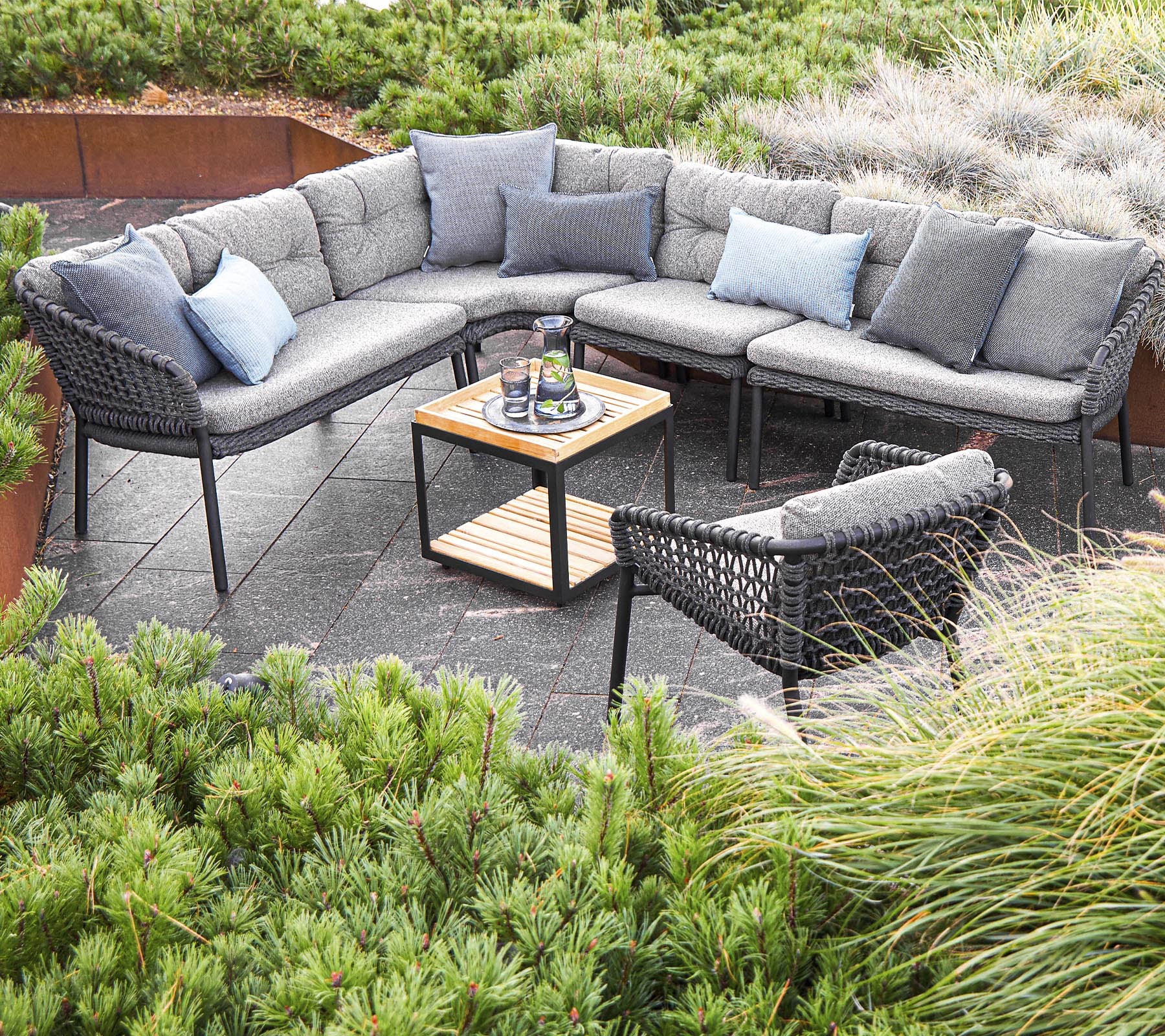 Agencement extérieur élégant avec un canapé sectionnel avec coussins et une table centrale, entouré de verdure.