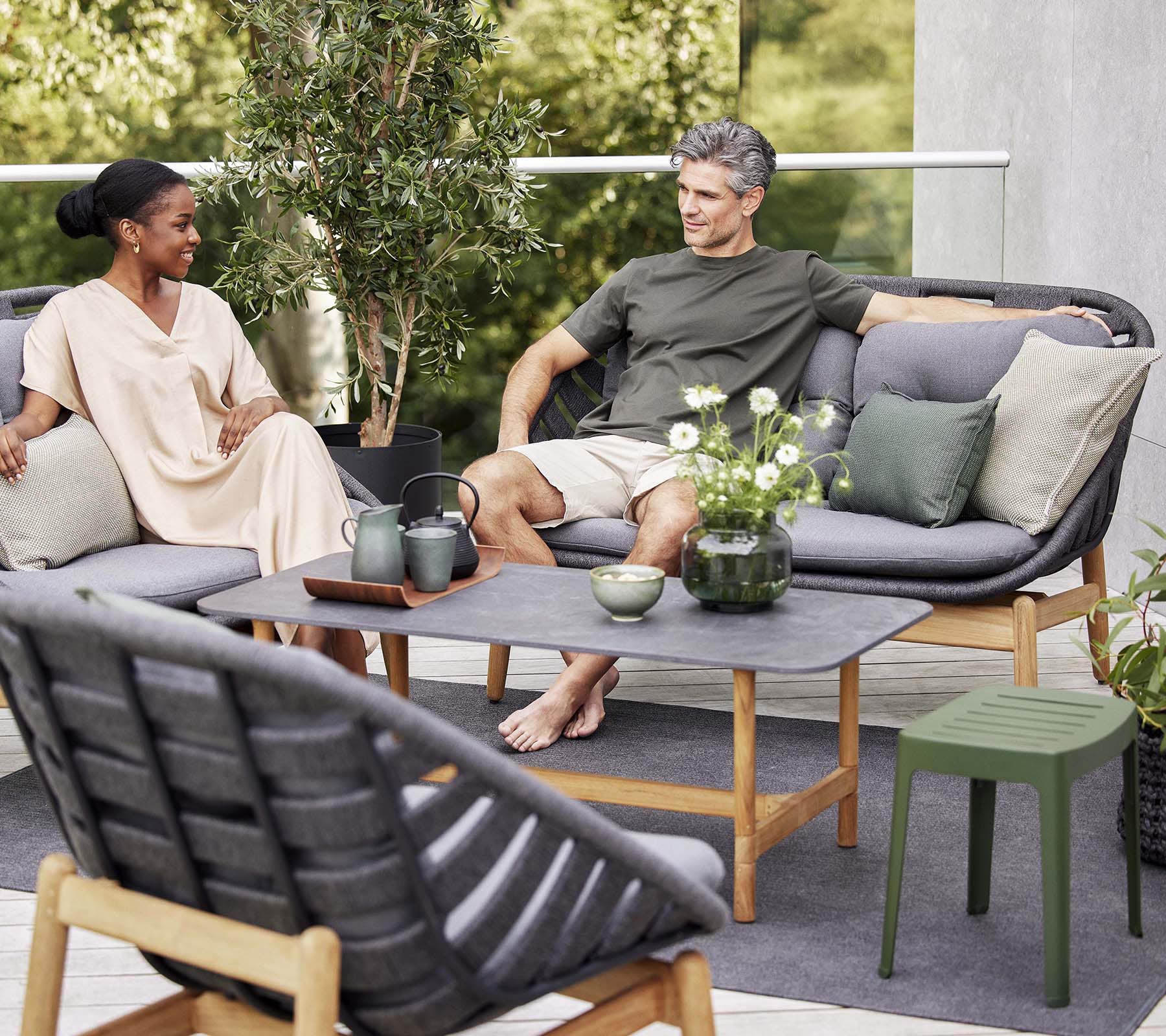 Un coin salon confortable avec un couple profitant de la conversation, entouré de verdure, avec des coussins doux et une table basse élégante.