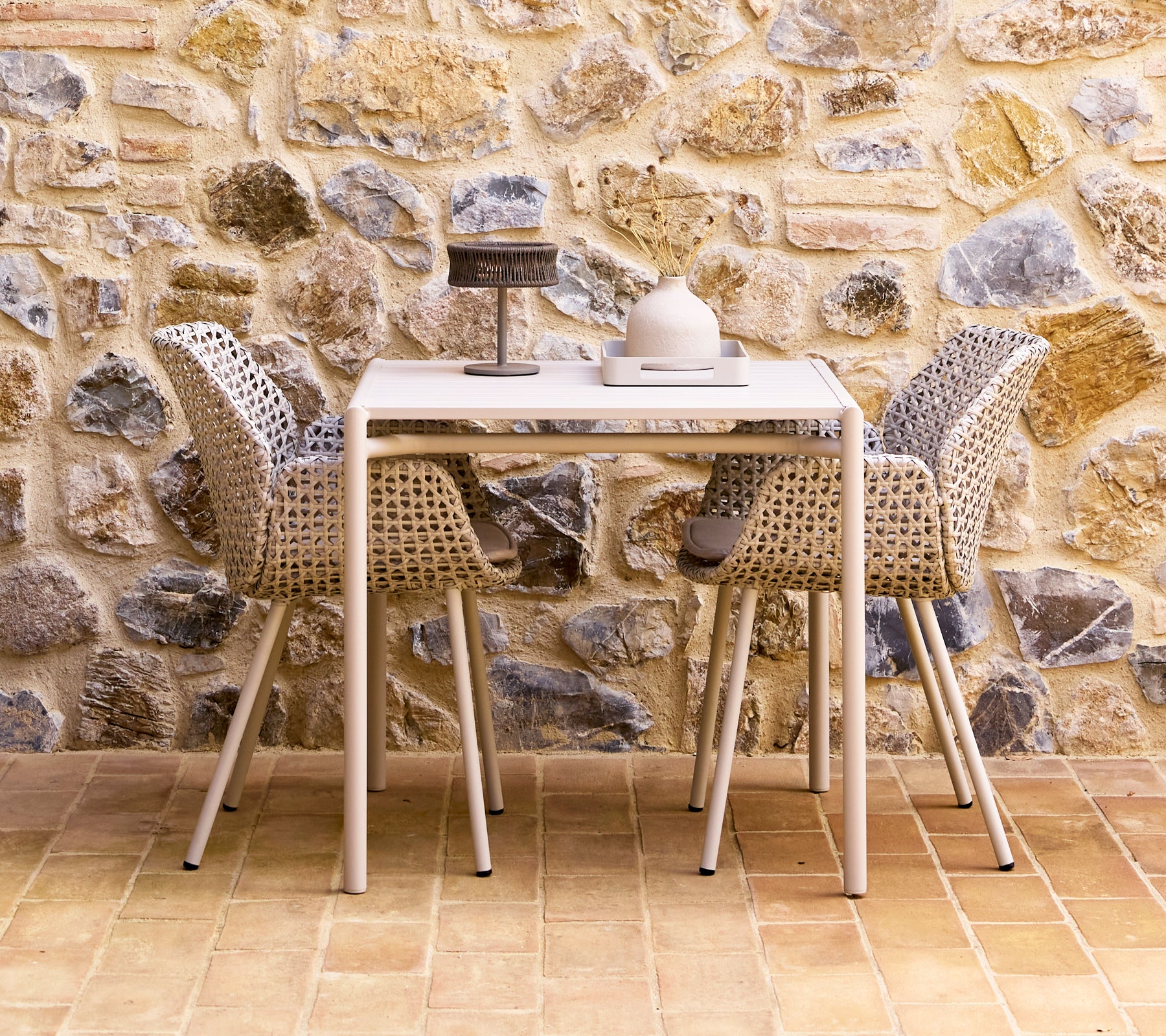 Un ensemble de salle à manger élégant avec des chaises de couleur sable disposées autour d'une table moderne, contre un mur en pierre texturé.